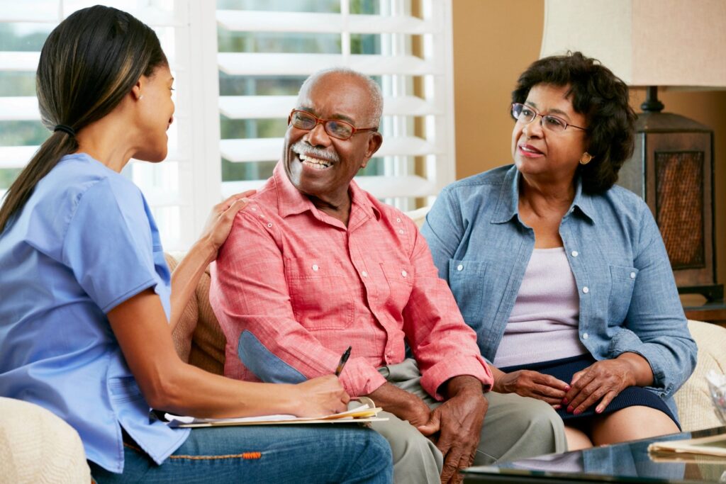 A healthcare worker talks with an elderly couple in a home setting.